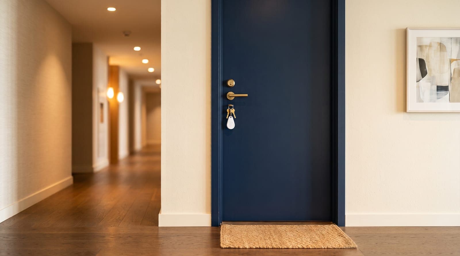 A navy condominium unit door in a modern corridor with keys and a white entry fob hanging in the lock